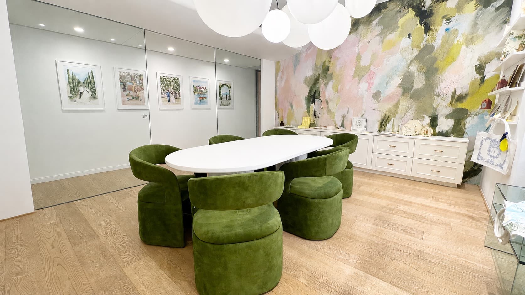 IuMi Studio in Milan: meeting room with olive green velvet chairs, an oval table, a painted mural wall and framed watercolour illustrations