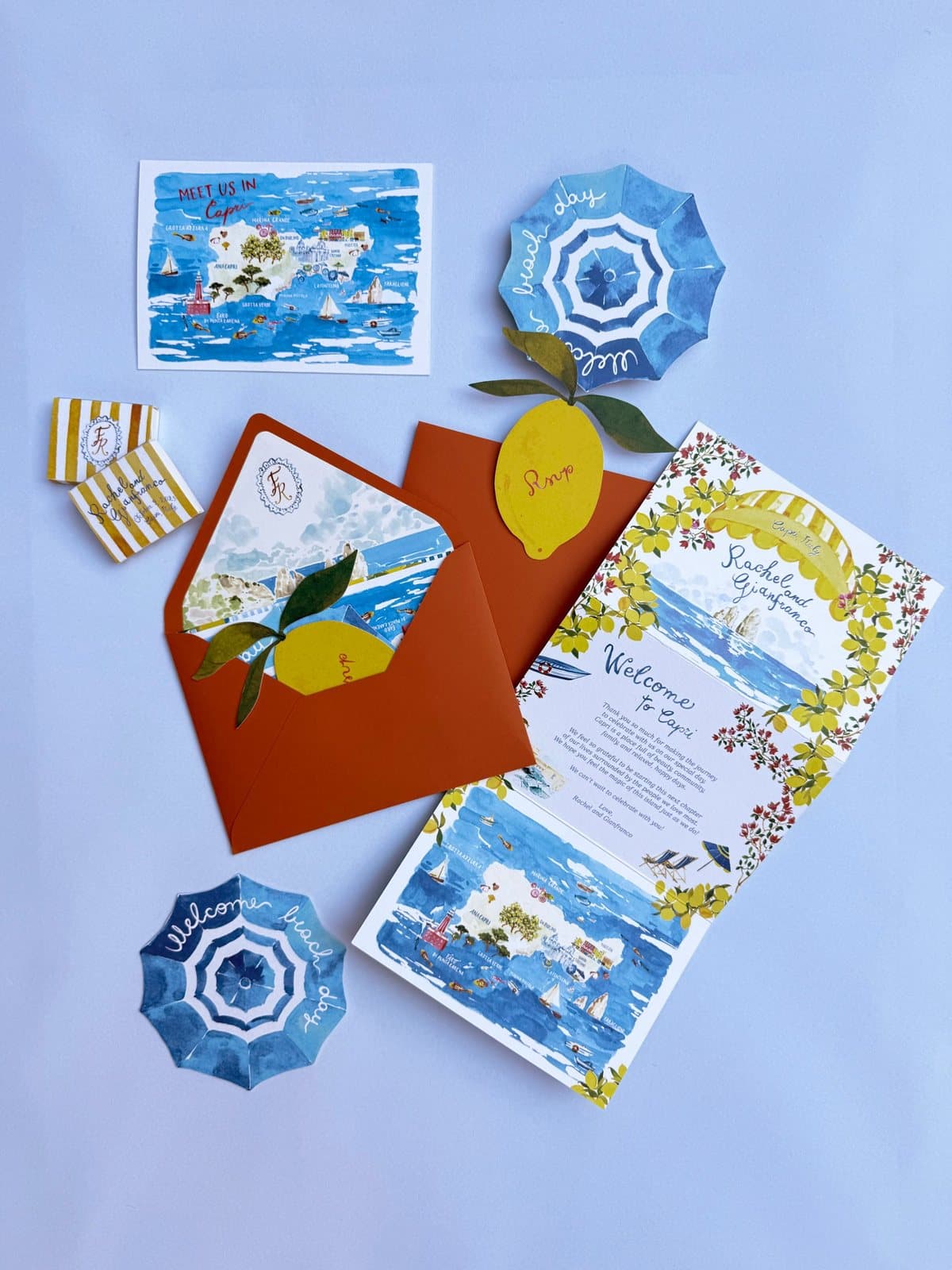 IuMi Studio invitation suite for a Capri wedding: illustrated map of the island, lemon-shaped RSVP card, beach umbrella welcome cards, terracotta envelope and lemon tree welcome booklet